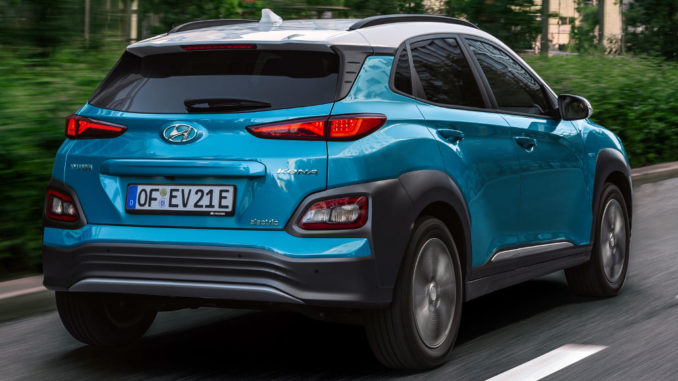 Ein türkiser Hyundai Kona Electric fährt 2018 auf einer Straße durch die Stadt.