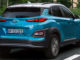 Ein türkiser Hyundai Kona Electric fährt 2018 auf einer Straße durch die Stadt.