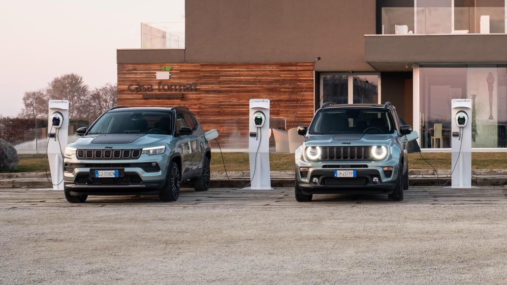 Ein silberner Jeep Renegade und Compass e-hybrid S stehen 2022 an Ladesäulen.