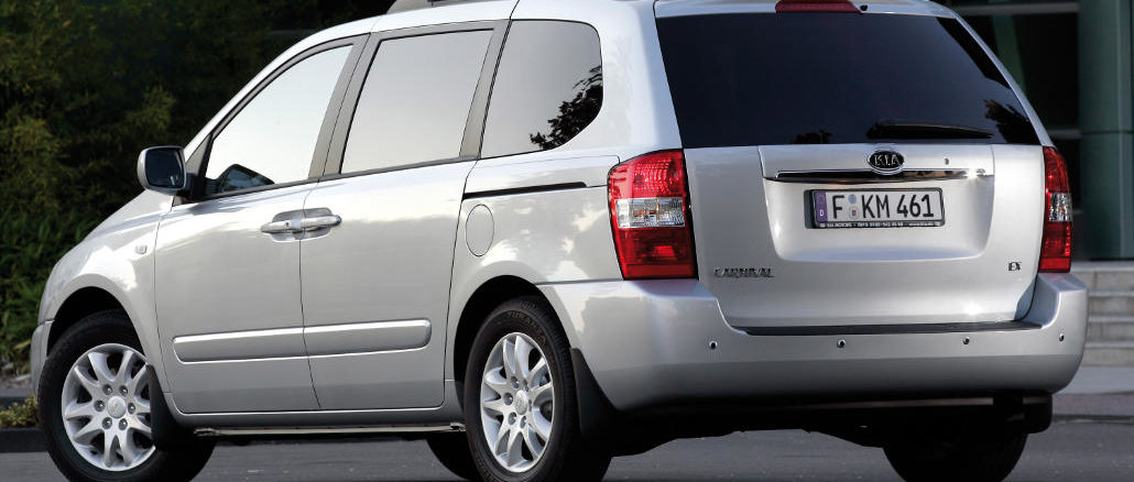 Ein silberner Kia Carnival steht vor einem Bürogebäude.