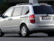 Ein silberner Kia Carnival steht vor einem Bürogebäude.