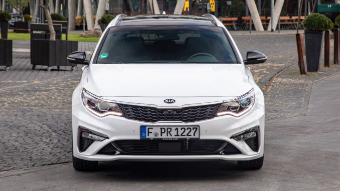 Ein weißer Kia Optima Sportswagon steht 2018 vor einer Fußgängerzone.