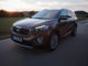 Ein brauner Kia Sorento fährt bei Sonnenuntergang auf einer Landstraße.