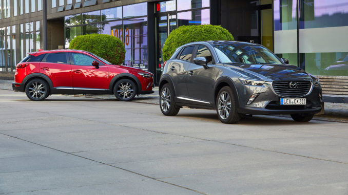 Ein roter und ein grauer Mazda CX-3 stehen 2017 vor einem Bürogebäude.