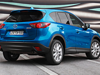 Ein blauer Mazda CX-5 steht 2012 auf einem Parkplatz vor einer bunten Plane.