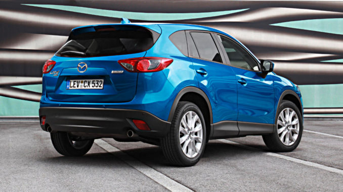 Ein blauer Mazda CX-5 steht 2012 auf einem Parkplatz vor einer bunten Plane.