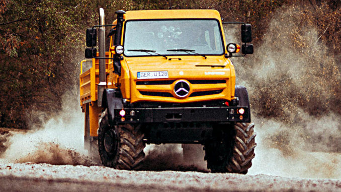 Ein orangener Mercedes Unimog fährt in einer Kiesgrube um die Kurve.