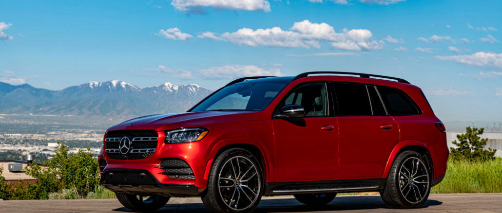 Ein Mercedes-Benz GLS 580 4MATIC, designo hyazinthrot metallic, Leder schwarz, steht 2019 auf einer Anhöhe vor einer Bergkette.