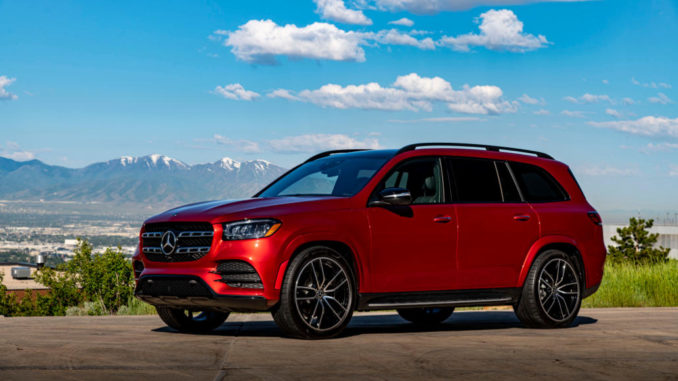 Ein Mercedes-Benz GLS 580 4MATIC, designo hyazinthrot metallic, Leder schwarz, steht 2019 auf einer Anhöhe vor einer Bergkette.