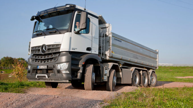 Ein weißer Mercedes-Benz Arocs 10x4/4 fährt auf hügeligem Gelände.