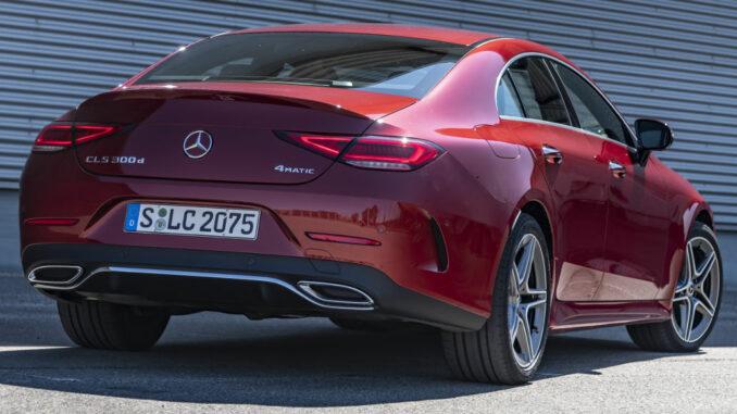 Mercedes-Benz CLS 300 d 4MATIC, Exterieur: designo hyazinthrot metallic, AMG Line; Leder Nappa schwarz, steht 2021 vor einer Wellblechwand.