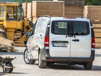 Ein silberner Mercedes Vito 116 CDI steht vor einem Holzstapel.