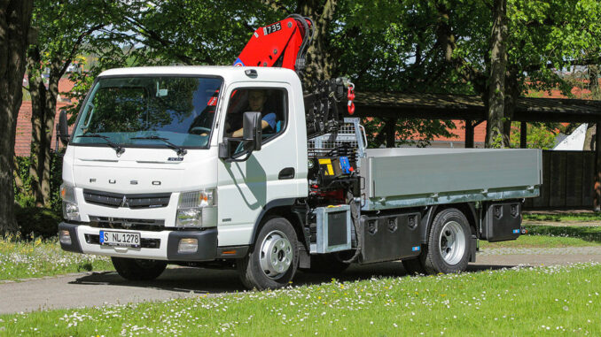 Ein weißer Mitusbishi Fuso Canter 7C15 HMF mit Ladekran fährt 2015 auf einen Friedhof.