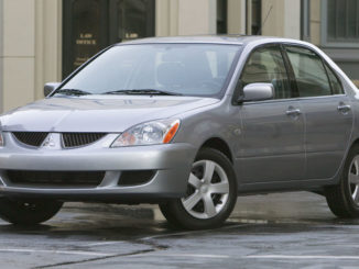 EIn silberner 2004 Mitsubishi Lancer LS steht in den USA vor einem Bürogebäude auf regennasser Straße.