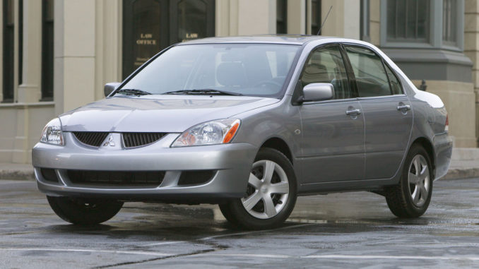 EIn silberner 2004 Mitsubishi Lancer LS steht in den USA vor einem Bürogebäude auf regennasser Straße.