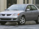 EIn silberner 2004 Mitsubishi Lancer LS steht in den USA vor einem Bürogebäude auf regennasser Straße.