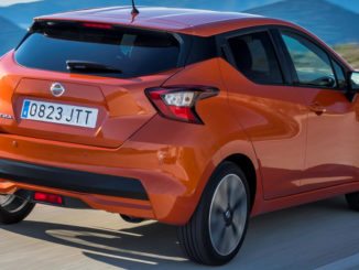 Ein orangener Nissan Micra fährt auf einer Höhenstraße am Meer entlang.