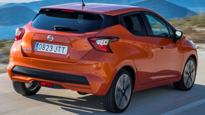 Ein orangener Nissan Micra fährt auf einer Höhenstraße am Meer entlang.