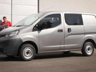 Ein grauer Nissan NV200 steht mit zwei Handwerkern auf einem Betriebshof.