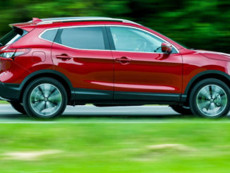 Ein roter Nissan Qashqai fährt 2018 über eine Landstraße am Waldrand.