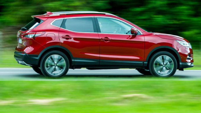 Ein roter Nissan Qashqai fährt 2018 über eine Landstraße am Waldrand.