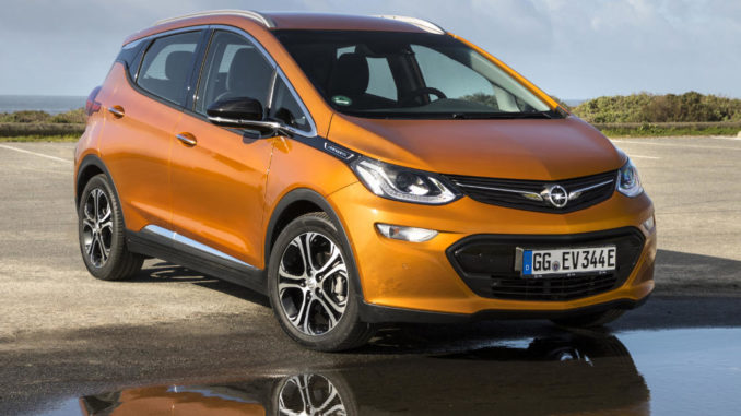 Ein rostfarbener Opel Ampera-e spiegelt sich in einer Pfütze.