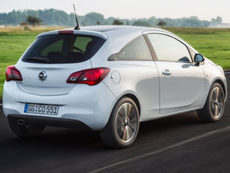 Ein weißer Opel Corsa E fährt in der Morgendämmerung über eine Landstraße.