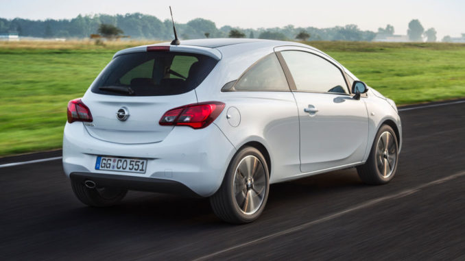 Ein weißer Opel Corsa E fährt in der Morgendämmerung über eine Landstraße.