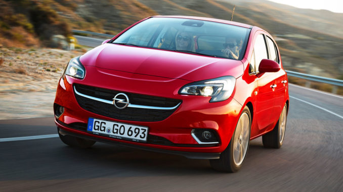 Ein roter Opel Corsa E fährt auf einer Landstraße durch eine mediterrane Landschaft.