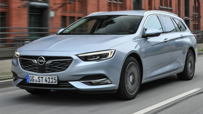 Ein hellblauer Opel Insignia B Sportstourer fährt an einem Backsteingebäude vorbei.