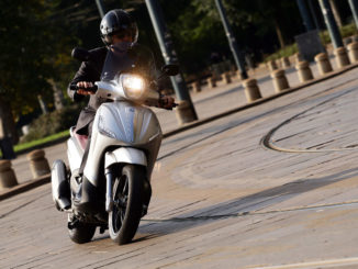 Eine beige Piaggio Beverly 350 fährt in einem Kreisverkehr.