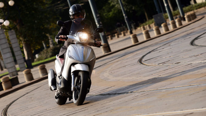 Eine beige Piaggio Beverly 350 fährt in einem Kreisverkehr.