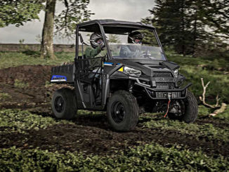 Ein Polaris Ranger EV fährt mit zwei Personen durchs Gelände.