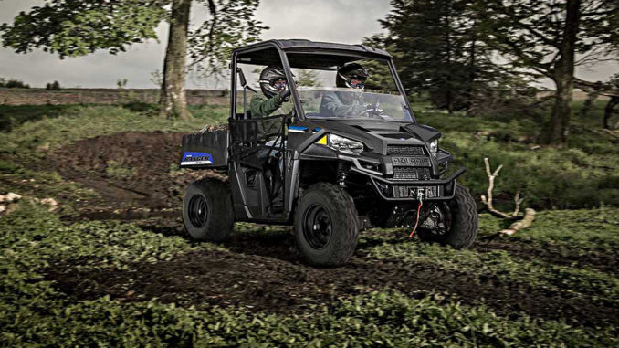 Ein Polaris Ranger EV fährt mit zwei Personen durchs Gelände.