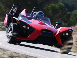 Ein roter Polaris Slingshot fährt auf einer Landstraße.