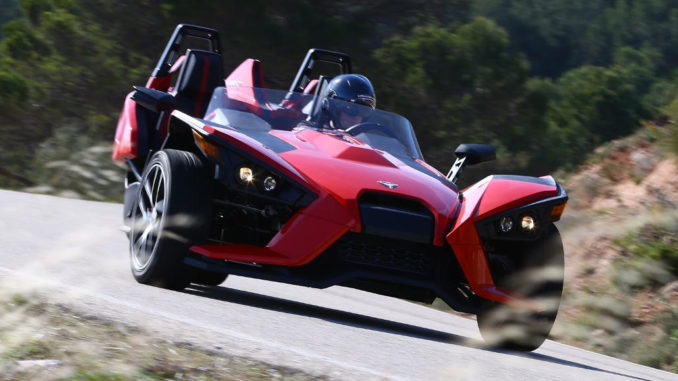 Ein roter Polaris Slingshot fährt auf einer Landstraße.