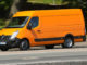 Ein orangener Renault Master fährt 2014 an einer Parkanlage entlang.