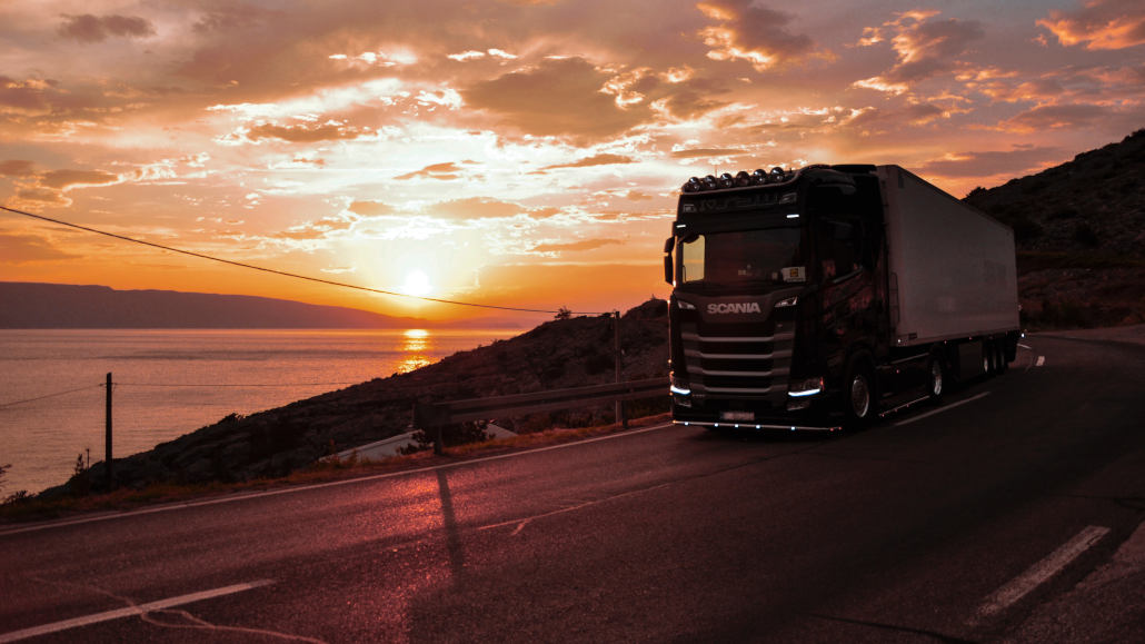 Ein Scania-Truck fährt 2022 auf einer Küstenstraße im Sonnenuntergang.