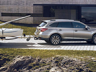 Ein silberner Subaru Outback mit Boot im Schlepp steht 2017 vor einem Betongebäude am Hafen.