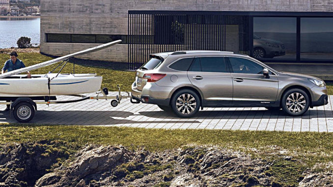 Ein silberner Subaru Outback mit Boot im Schlepp steht 2017 vor einem Betongebäude am Hafen.