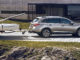 Ein silberner Subaru Outback mit Boot im Schlepp steht 2017 vor einem Betongebäude am Hafen.