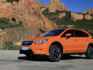 Ein orangener Subaru XV steht 2012 vor ockerfarbenen Felsen.