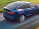 Ein blauer Tesla Model X fährt auf einer Landstraße.