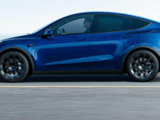 Ein blauer Tesla Model Y der ersten Generation fährt auf einer Küstenstraße.