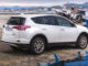 Ein weißer Toyota RAV4 Hybrid steht 2016 an einem kleinen Mittelmeerhafen zwischen Schiffen.