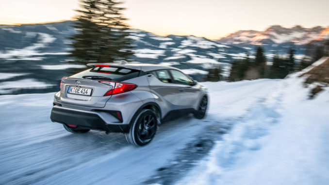 Ein silberner Toyota C-HR bremst auf schneeglatter Landstraße in den Alpen.