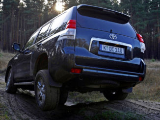 Ein dunkelblauer Toyota Landcruiser 150 fährt 2011 durch unwegsames Gelände im Wald.