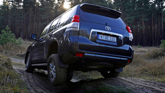 Ein dunkelblauer Toyota Landcruiser 150 fährt 2011 durch unwegsames Gelände im Wald.