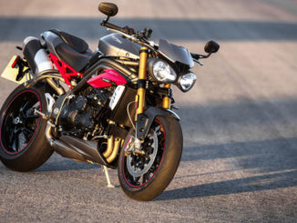 Eine graue Triumph Speed Triple R mit roten Karosserieteilen abgestellt auf einer Straße im Sonnenuntergang.