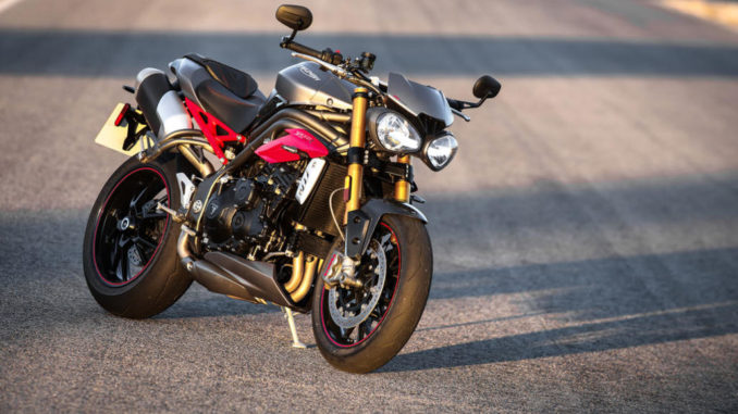 Eine graue Triumph Speed Triple R mit roten Karosserieteilen abgestellt auf einer Straße im Sonnenuntergang.